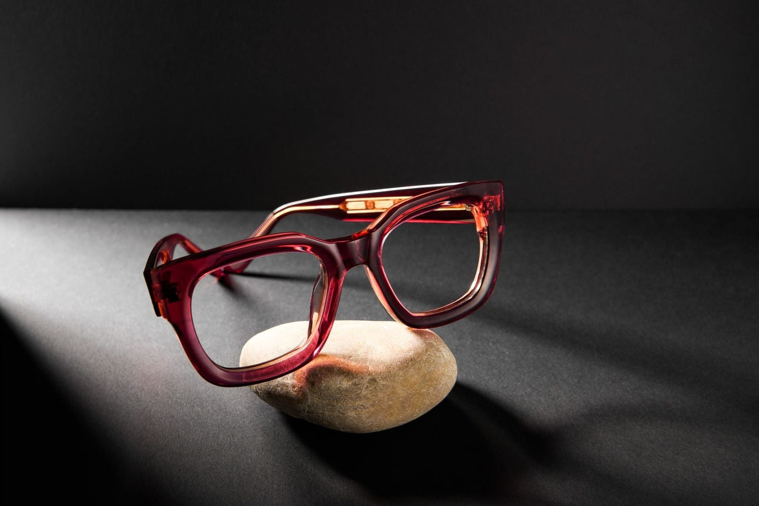 Cubo Eyewear Dee frame in pink acetate displayed on a stone against a dark background