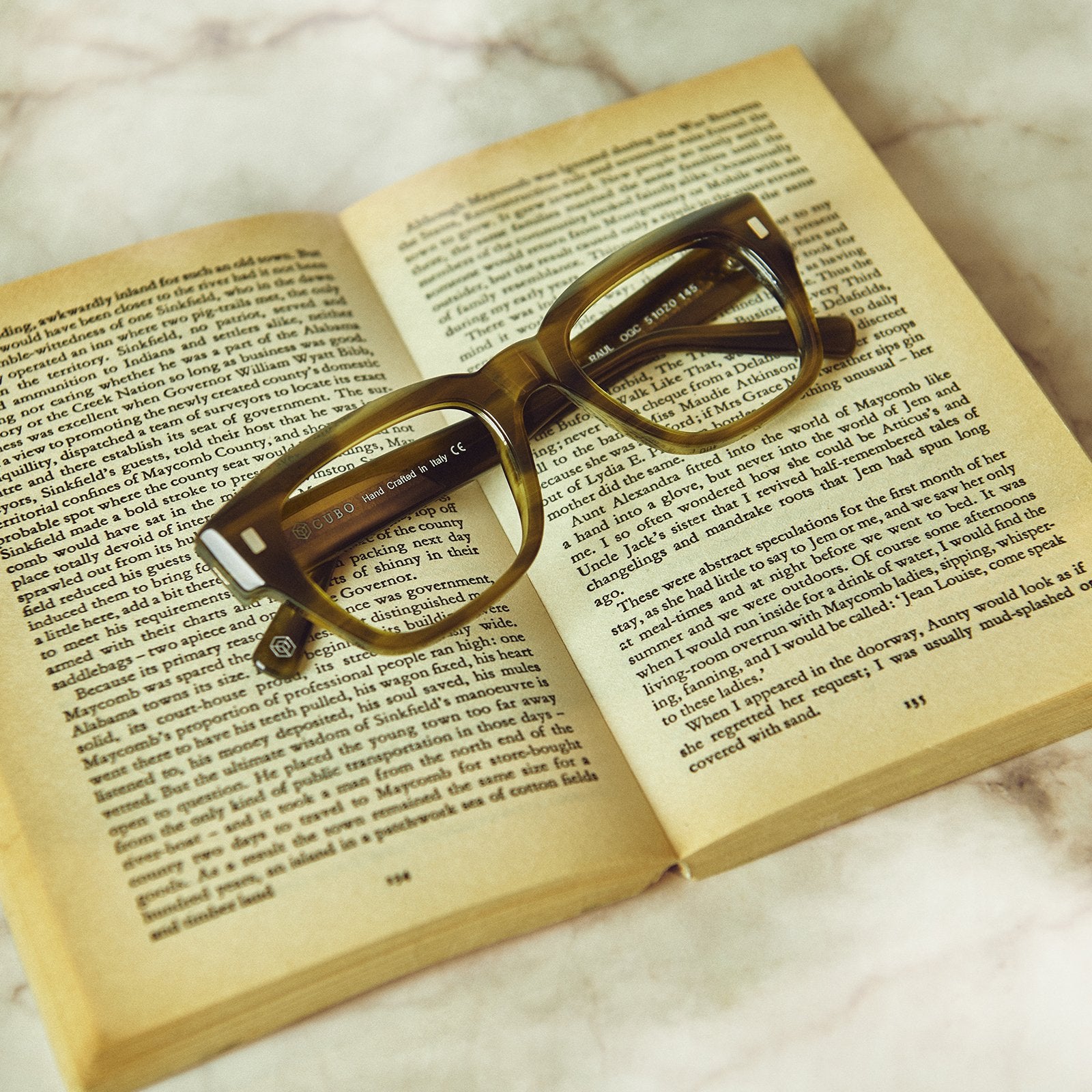 Cubo Eyewear green acetate glasses resting on an open book in a lifestyle reading scene